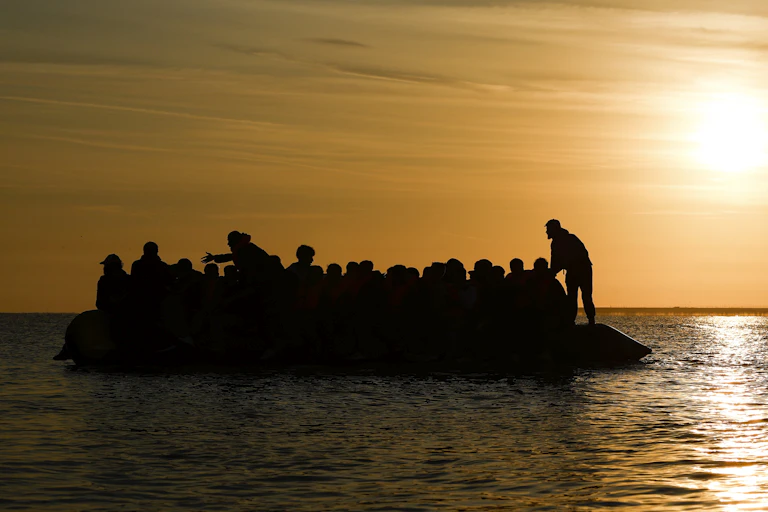 At sunset, dozens of people board a small inflatable boat in the water off the coast of France
