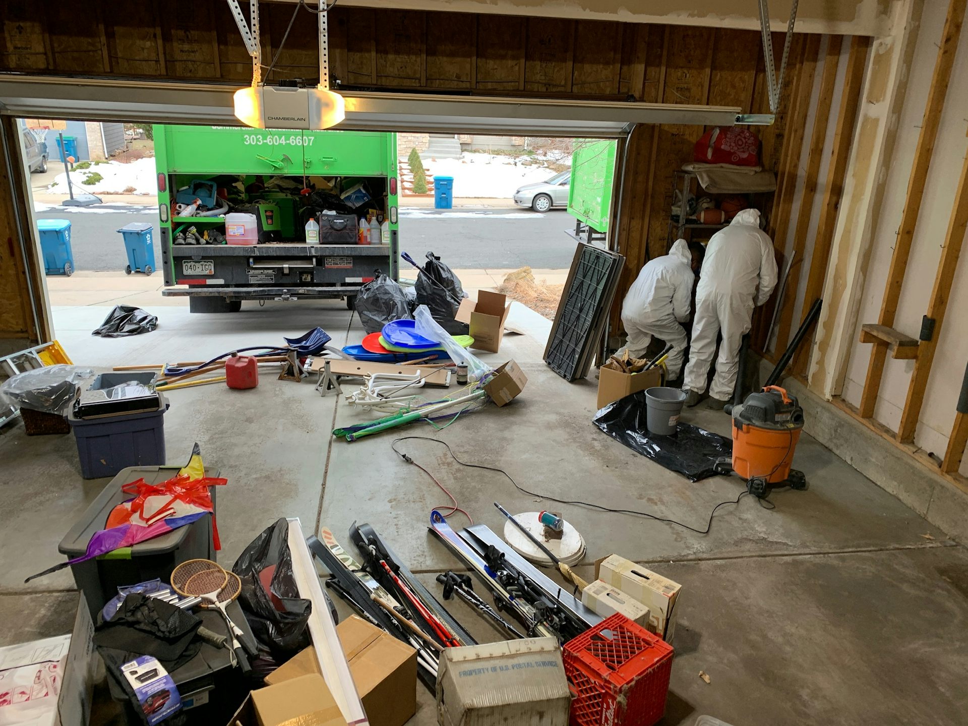 Two workers in white coverall suits clean a garage affected by smoke from the Marshall Fire.
