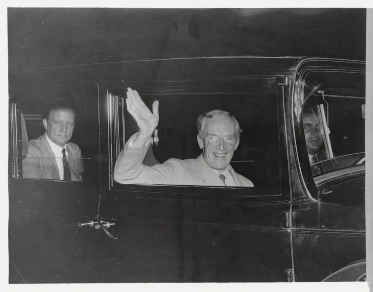 A man waves through the window of a black car.