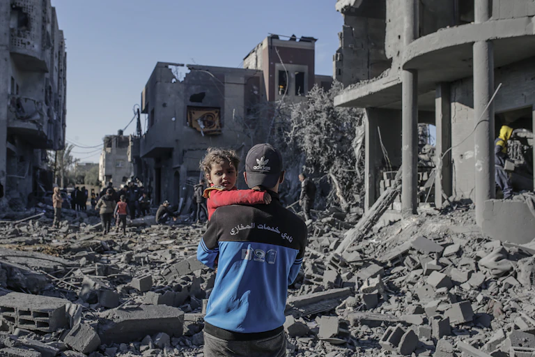 A man holding a small child surrounded by ruined buildings in Gaza.