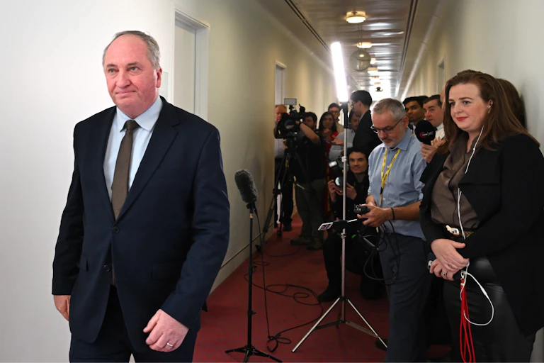 Man in a dark suit walks away from press pack