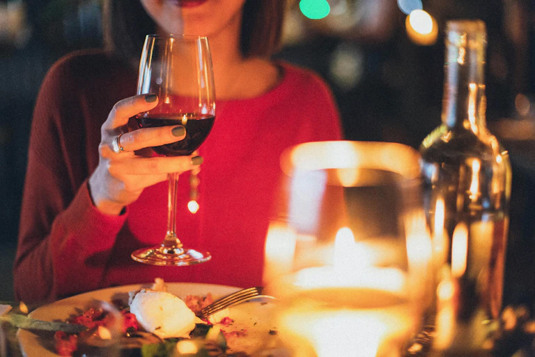 Woman holding glass red wine, glass white wine and bottle in foreground