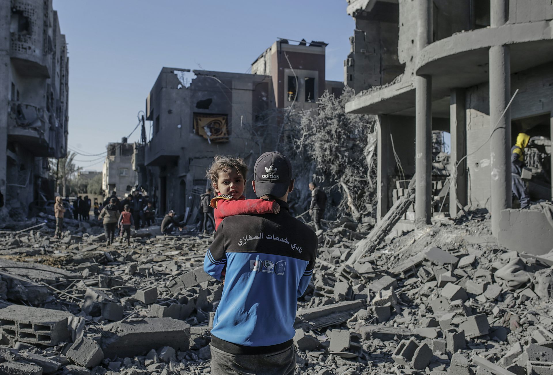 A man holding a small child surrounded by ruined buildings in Gaza.