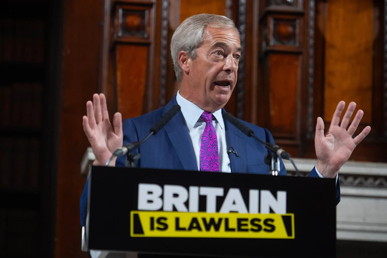 Nigel Farage gestures with his hands while speaking at a podium that reads 'britain is lawless'
