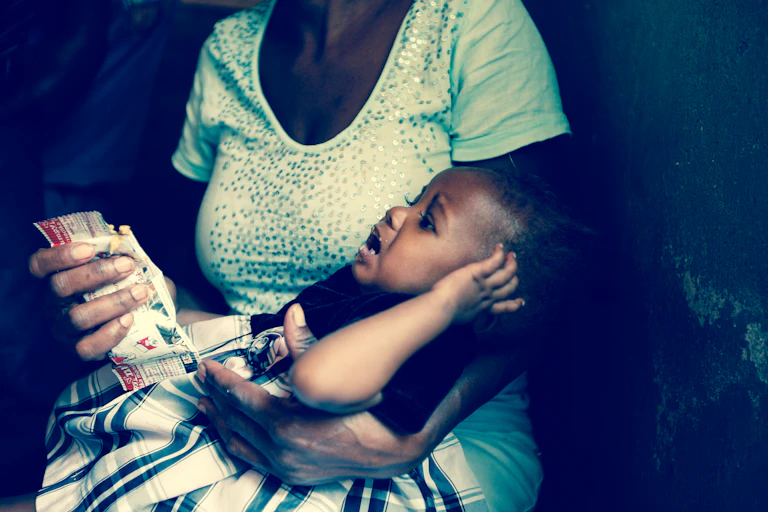 A woman cradling a crying baby on her lap while holding a high-nutrient food pack