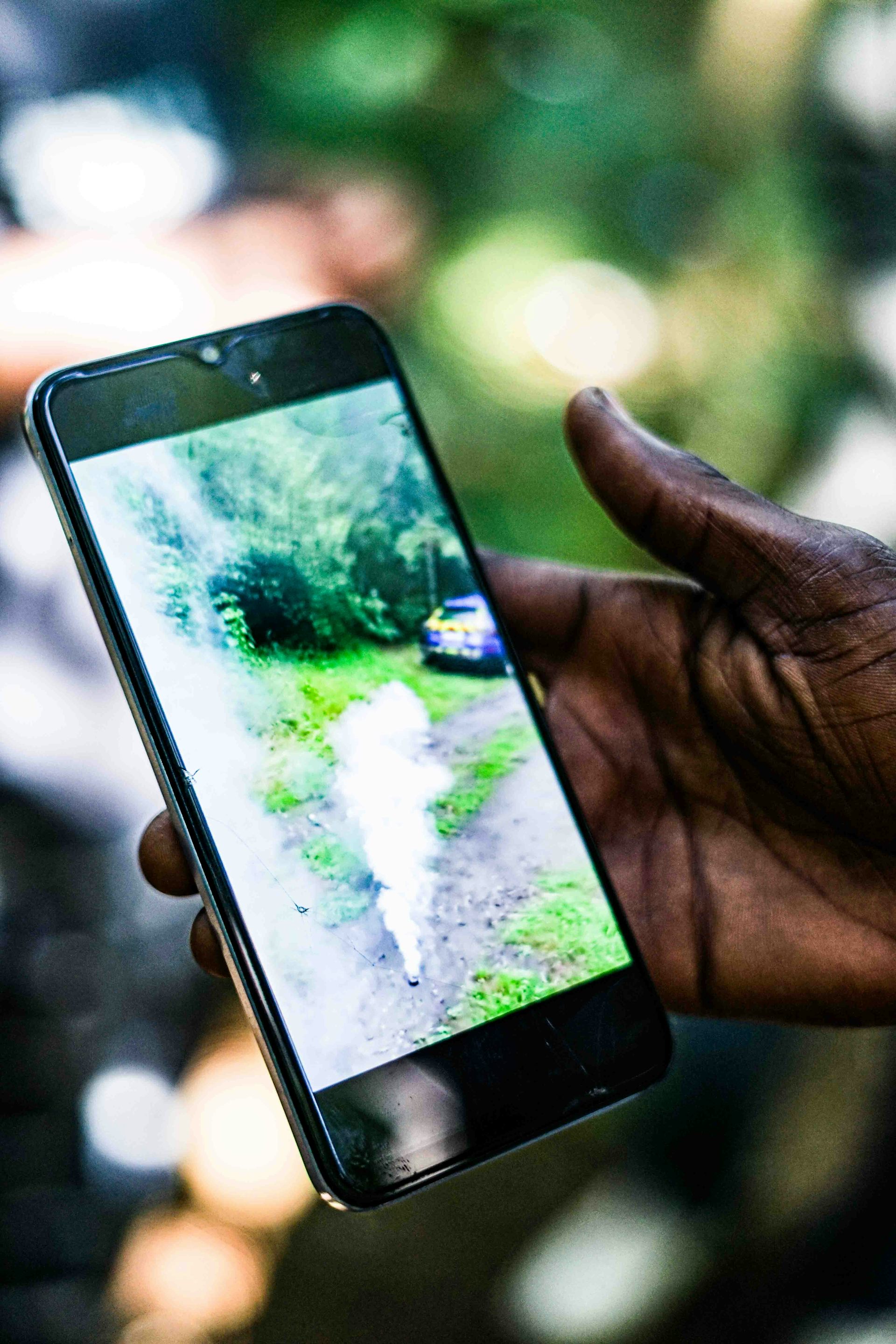 A hand holding an iphone that shows a gas canister deploying gas on a forest floor