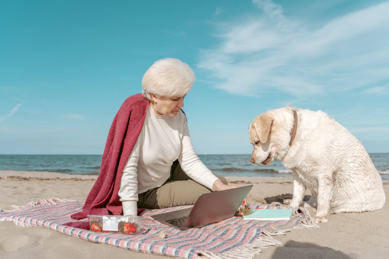A dog and its owner on a beach, seemingly both looking at the same laptop screen in puzzlement.