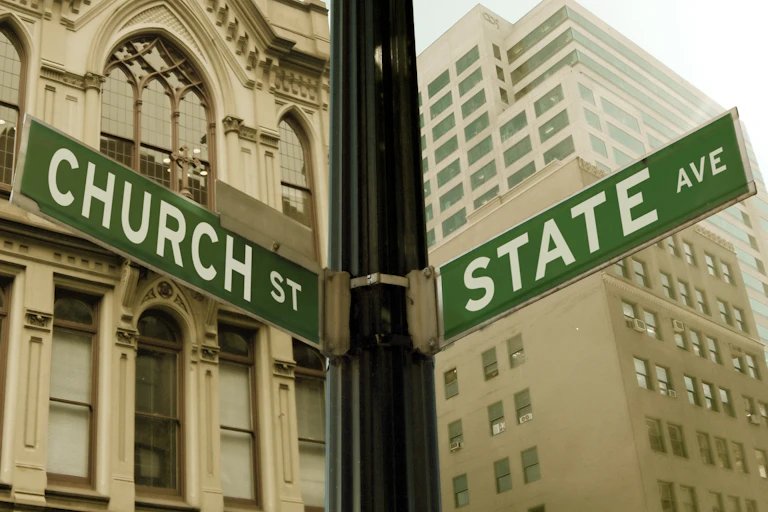 An intersection in front of two tall, tan buildings has signs for 'Church St' and 'State Ave.'