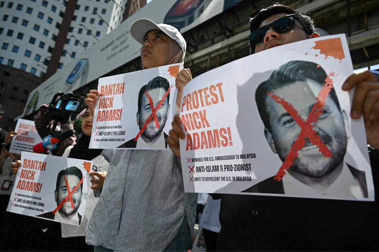 People hold placards with a red cross over a man's face.