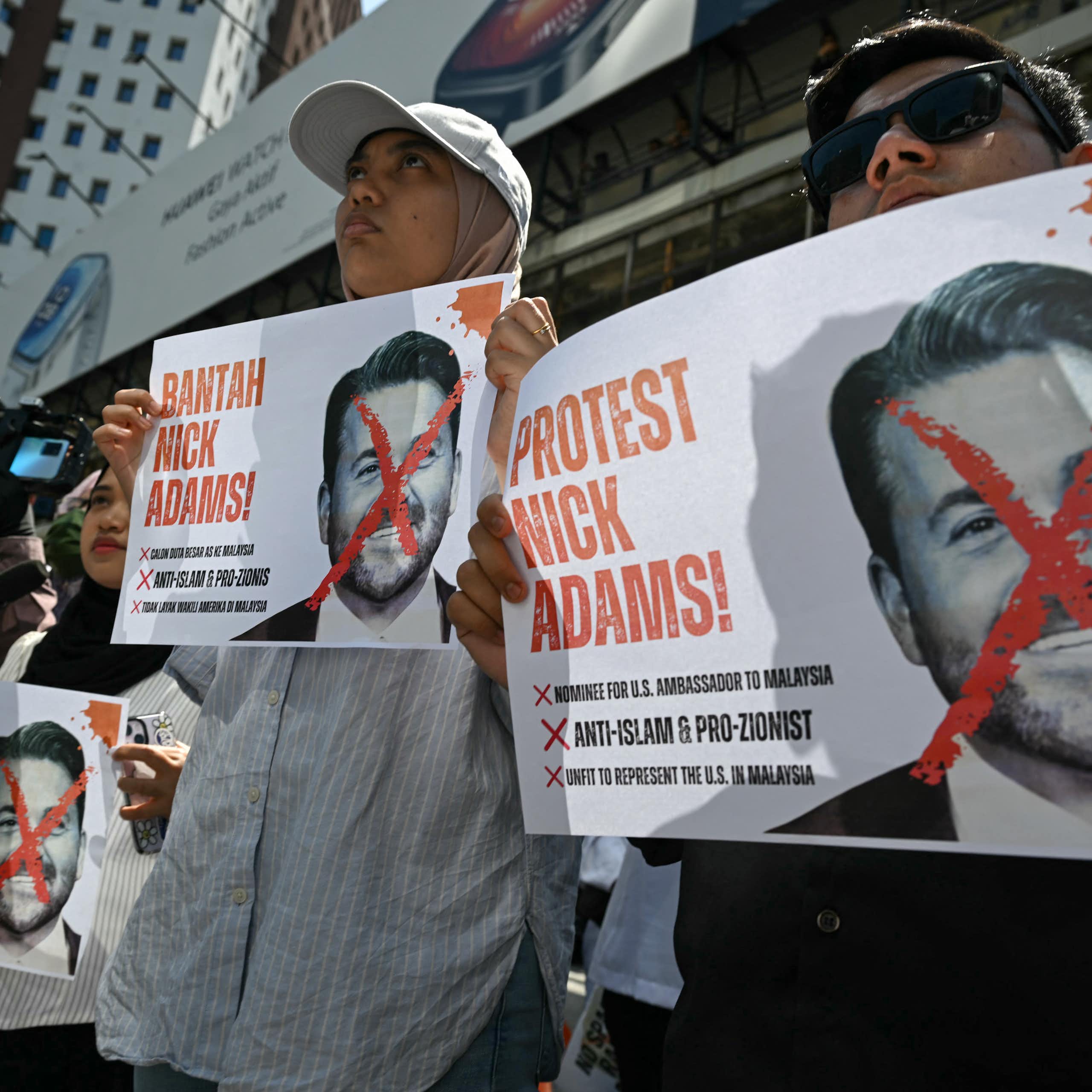 People hold placards with a red cross over a man's face.