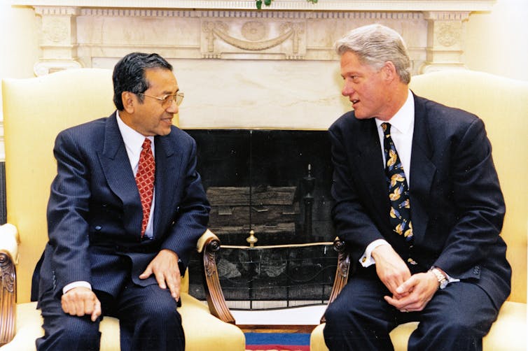 Two men in suits sit and chat.
