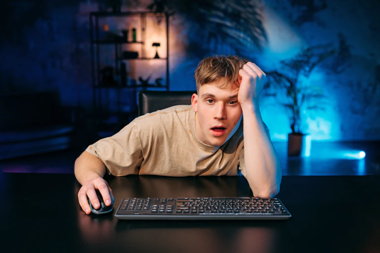 Joven con gesto de aburrimiento frente a un ordenador