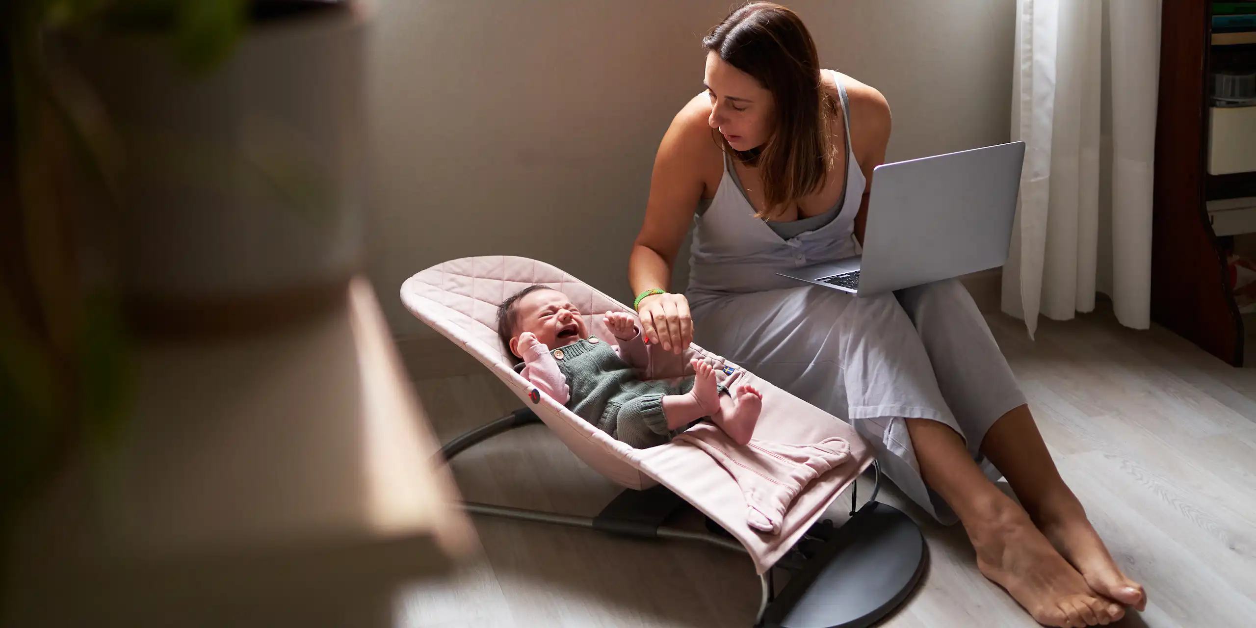 woman with laptop comforts a crying baby in a seat