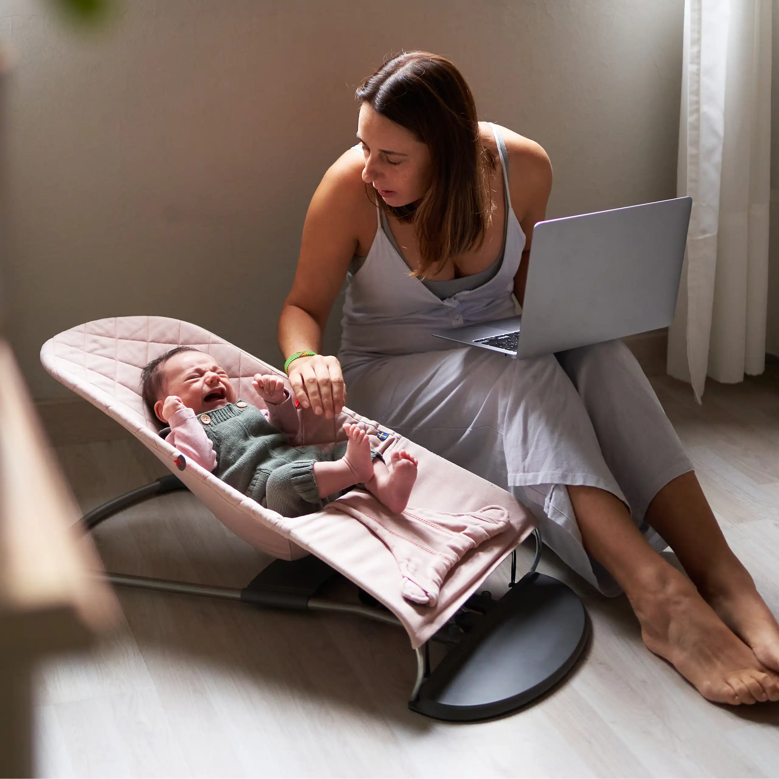 woman with laptop comforts a crying baby in a seat