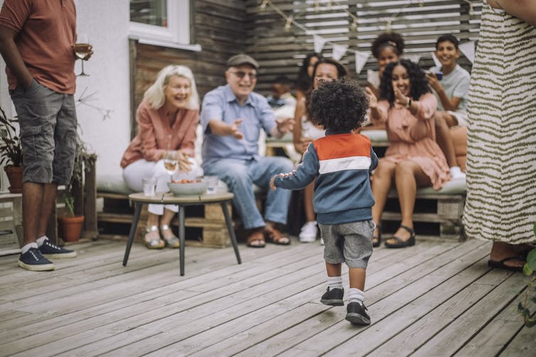 small boy runs away from camera toward extended family at a party