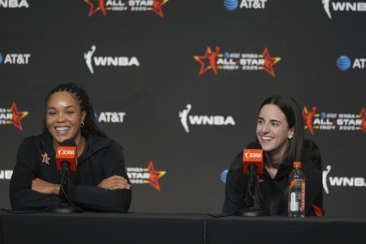 Black Woman se sienta junto a las mujeres blancas en la mesa de conferencias frente al fondo con el logotipo de VNBA