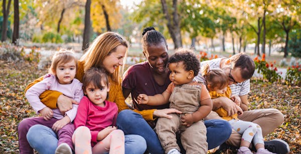 three adults hold four toddlers on their laps outside