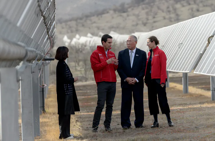 Three people talk under the shade of solar panels.