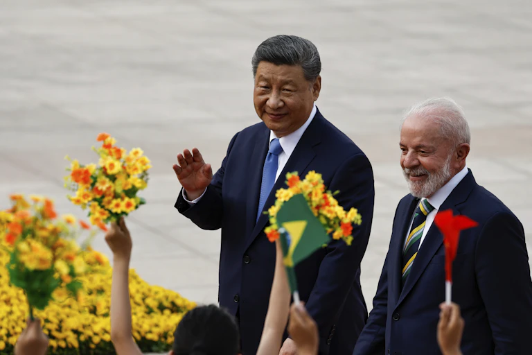 Two men wave to a crowd as they walk past people holding out flowers.