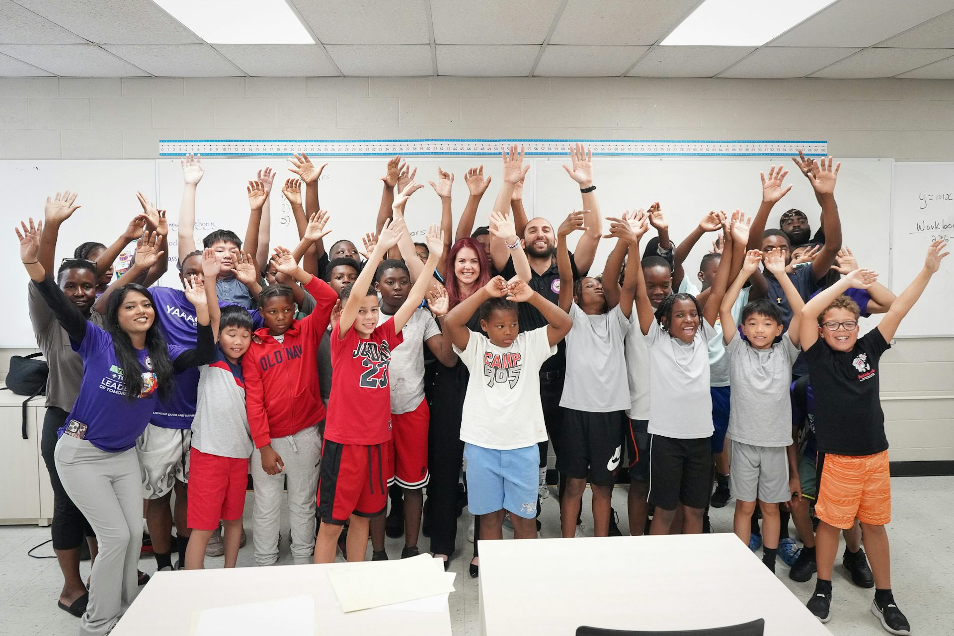 Students stand in a group with arms raised.