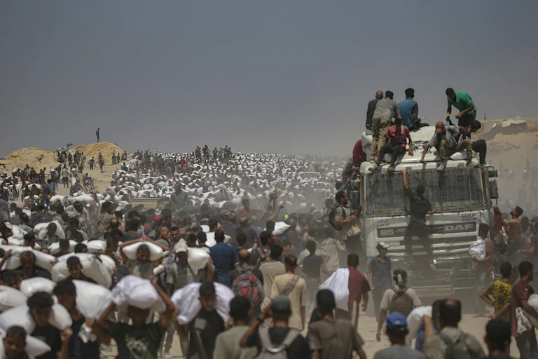 Thousands of Palestinian civilians carrying aid from a truck.