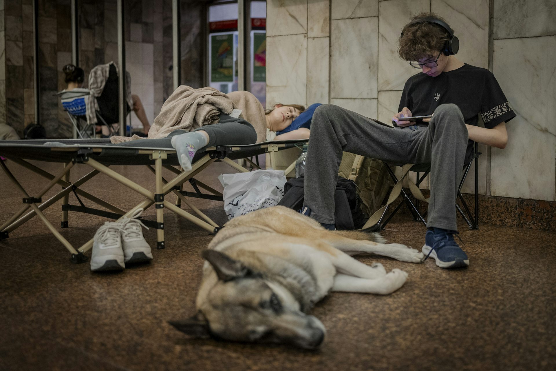 El joven está sentado en la estación de metro con su perro durmiendo sobre sus pies.