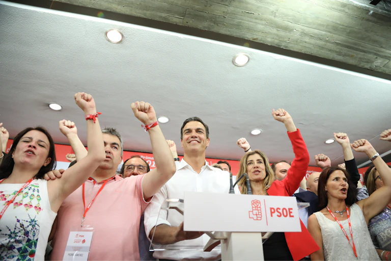 Varias personas con el puño en alto detrás del atril con el logotipo del PSOE