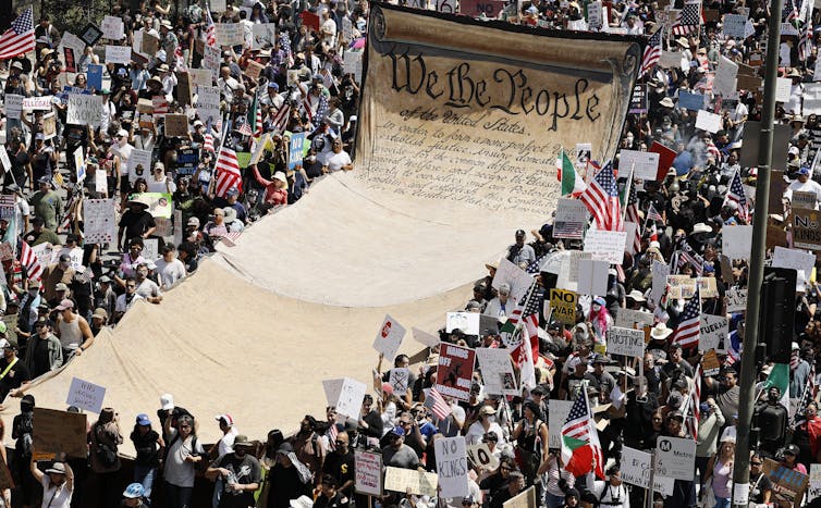 A crowd supports a long banner imprinted with the opening lines of the US Constitution.