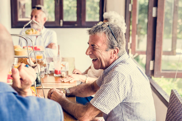 Older man laughs with friends at morning tea