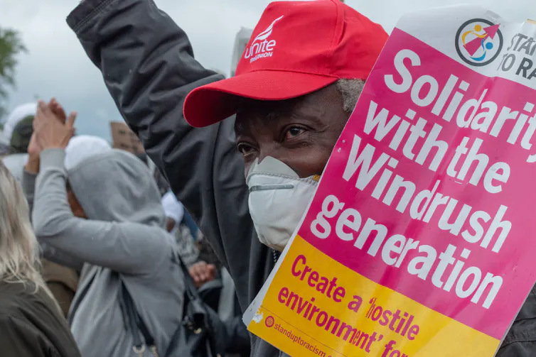 A man at a protest holding a sign that reads 'solidarity with the Windrush generation'