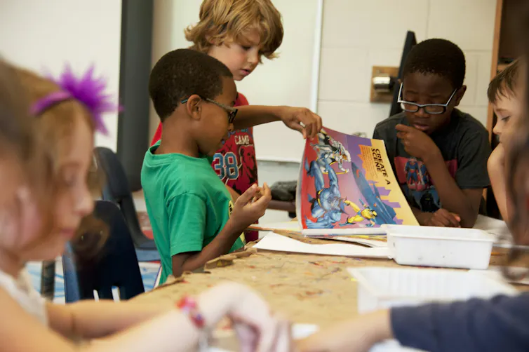 A group of children colour at a brown paper-covered table