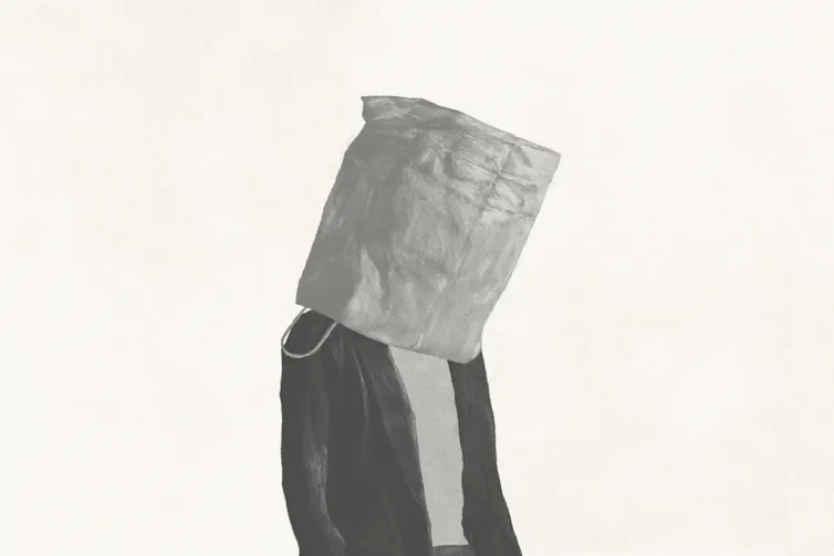 A man walks with a paper bag on his head.