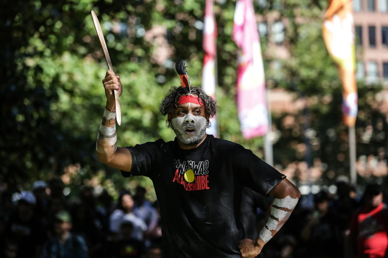 An Aboriginal man outside in ceremonial paint and an Aboriginal flag t-shirt