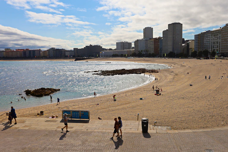 Una playa urbana con edificios de fondo y personas caminando en primer plano