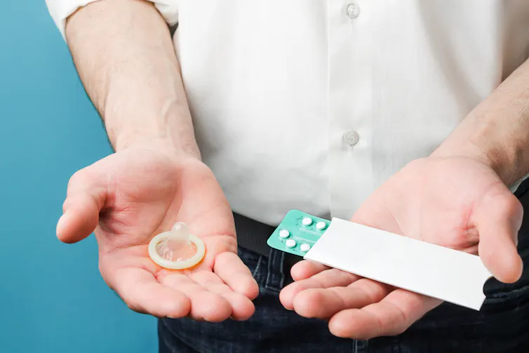A man holds a condom in one hand and a blister pack of birth control pills in the other.