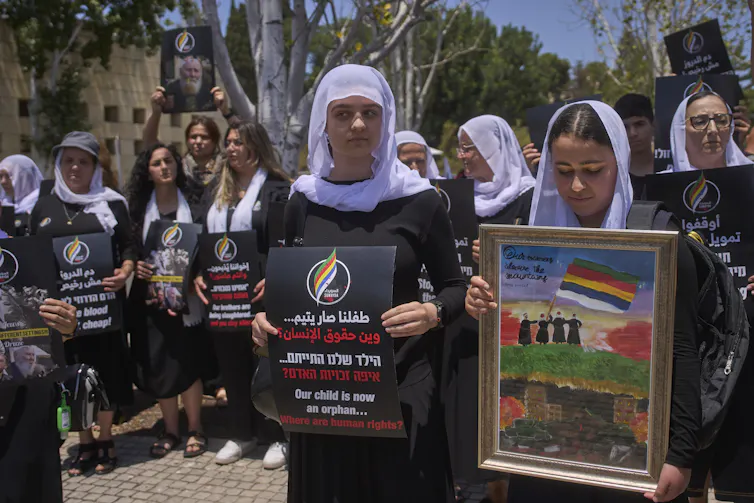 Women with head scarves hold banners at a protest.
