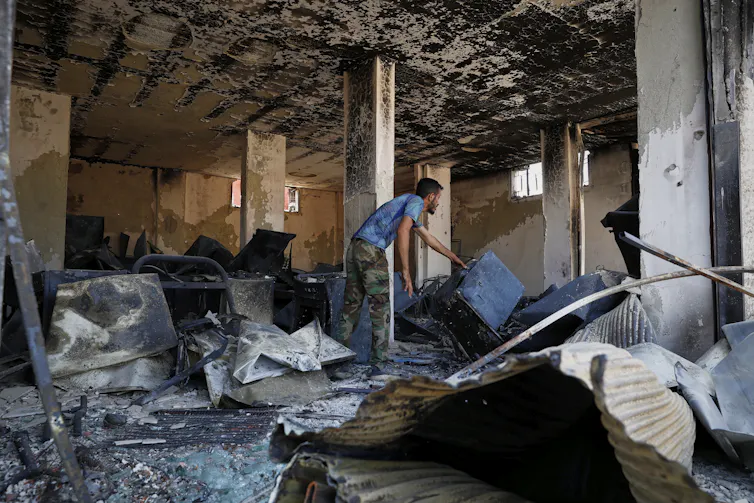 A man in a blue T-shirt cleans up amid rubble.