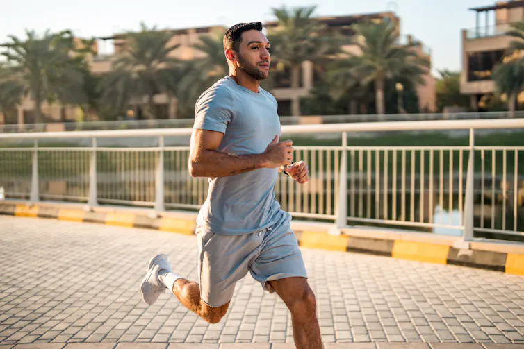 Un hombre corriendo al aire libre por un camino pavimentado rodeado de palmeras y edificios.