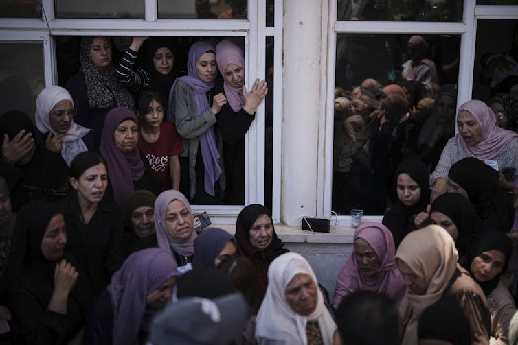 A crowd of women in dresses and headscarves look out of open windows.