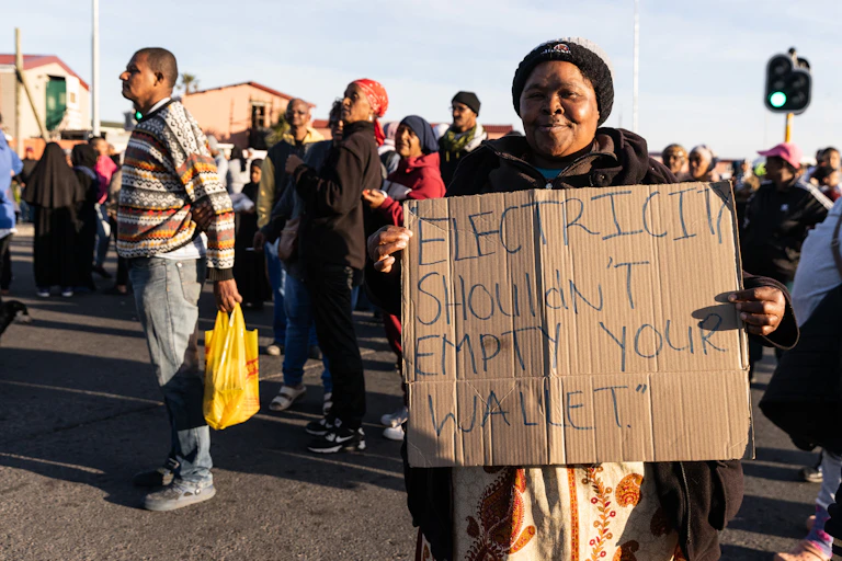 A woman holds up a sign at a protest saying "Electricity shouldn't empty your wallet"