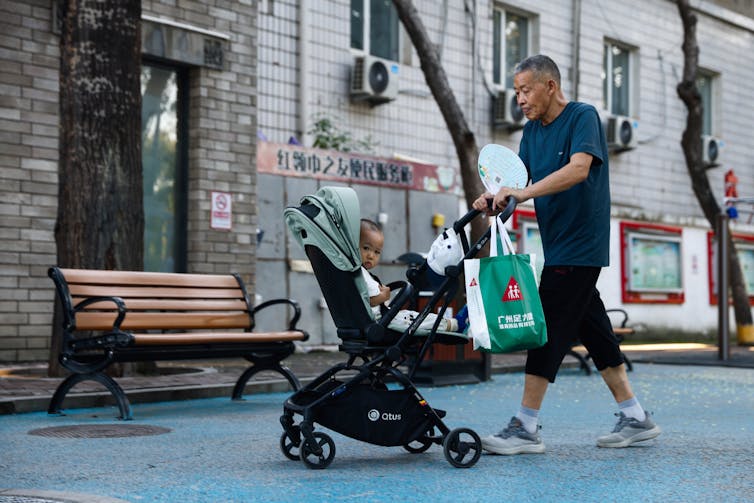 An elderly Chinese man pushing a baby along in a stroller.
