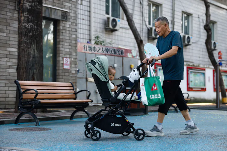 An elderly Chinese man pushing a baby along in a stroller.