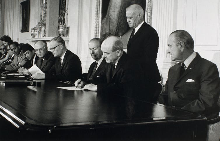 People sit at a large table and sign documents.