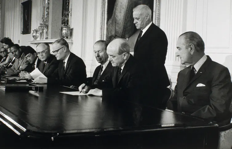 People sit at a large table and sign documents.