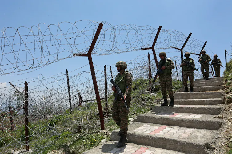 Armed soldiers walk next to a barbed-wire fence.