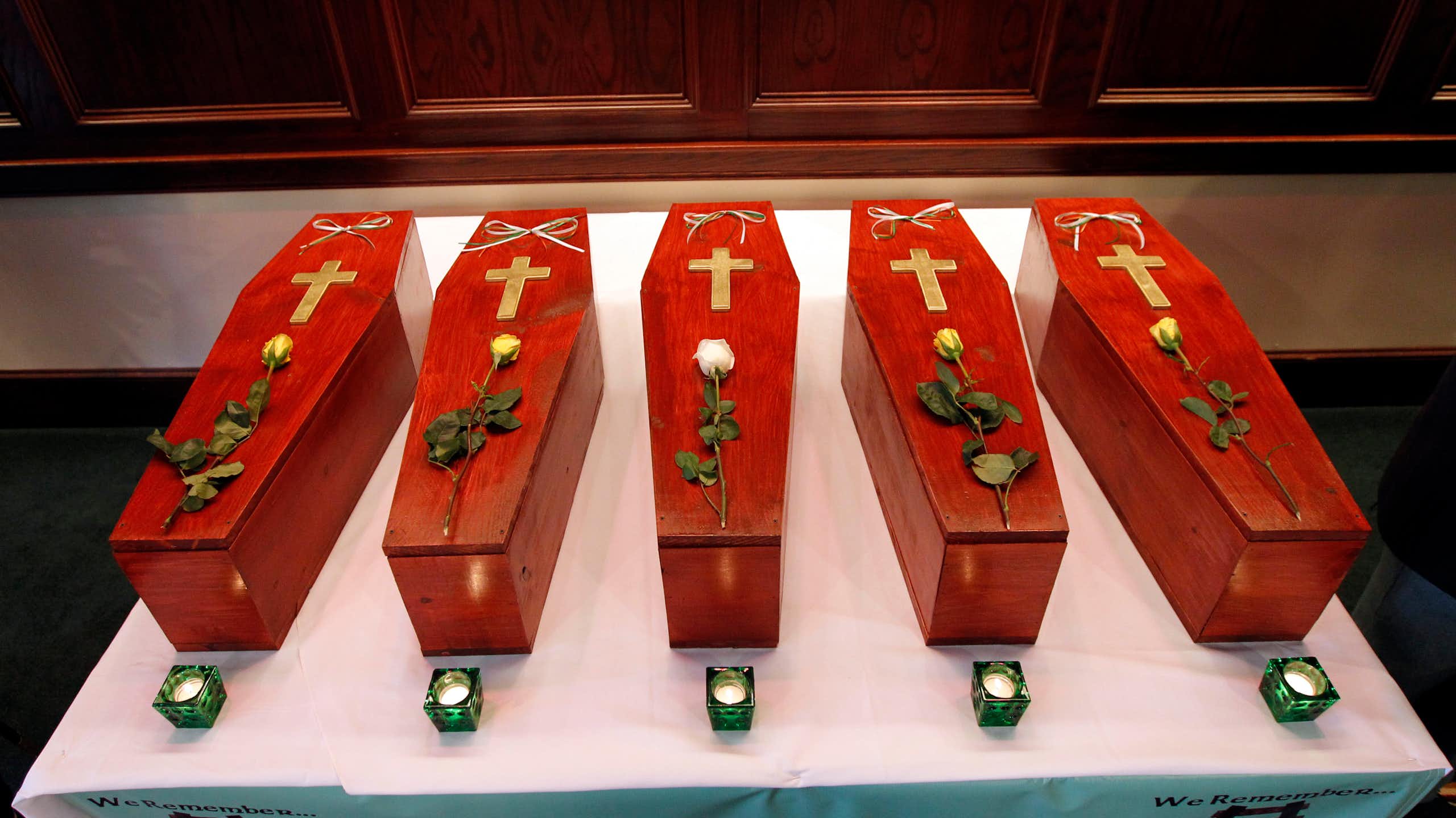 Row of five small red caskets with a cross and rose on top of each