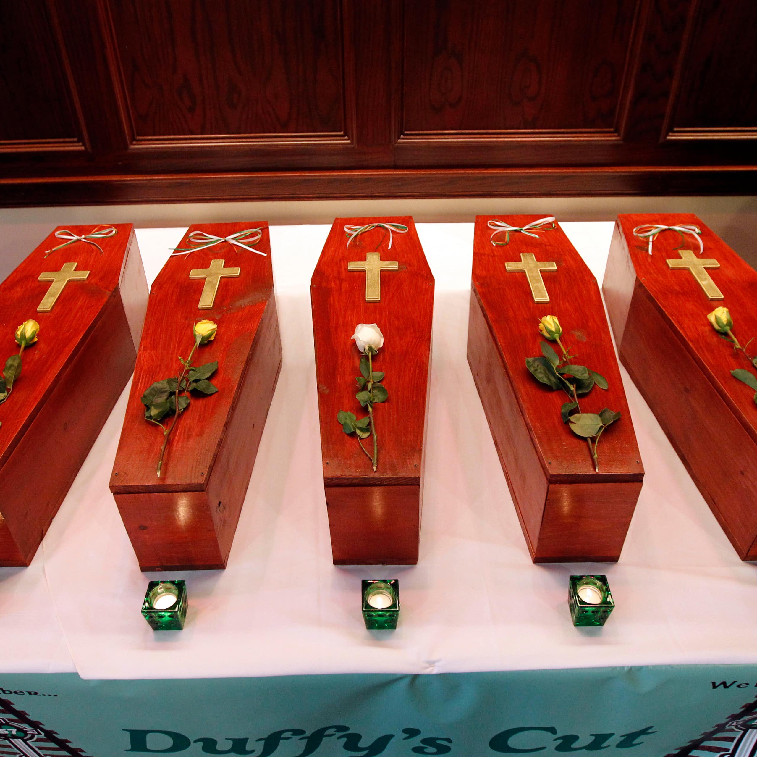 Row of five small red caskets with a cross and rose on top of each