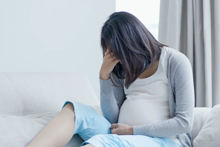 Pregnant woman sitting on a couch with her face in her hands in a sad posture