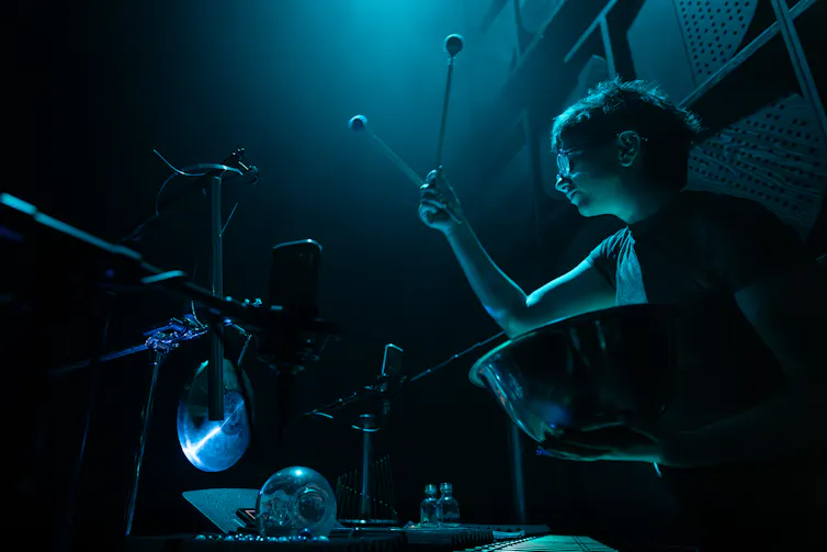 Under a blue light, a woman holds up mallets.