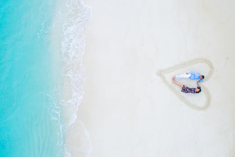 Una pareja en la arena de la playa rodeados de un corazón